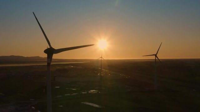 Sagome di pale eoliche che girano al tramonto in citt&agrave;. Sfondo anonimo del cielo.