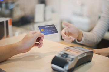 Hand of man customer using wireless or contactless payment of a credit card. Young Asian cashier or seller are smiling to accept payment by nfc technology at retail shop. Contactless payment concept.