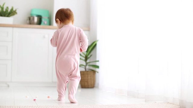 cute little baby girl walking around the room, one year old