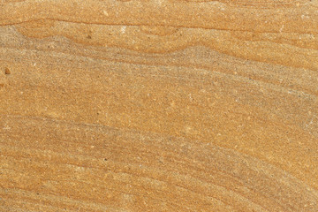 The surface of the cliff of yellow and brown sandstone on the seashore, weathered and faded in the sun.