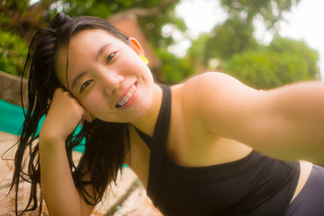 holidays lifestyle - young beautiful and happy Asian Korean woman in bikini enjoying vacation trip relaxed and blissful taking selfie photo at tropical resort swimming pool