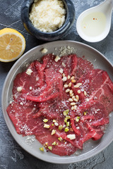 Above view of carpaccio beef with seasonings on a grey plate, vertical shot, close-up