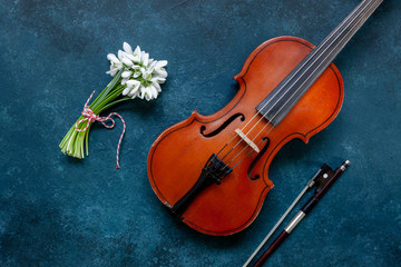 Fototapeta na wymiar Old Violin and Fresh beautiful bouquet of the first spring forest snowdrops flowers with red and white cord martisor - traditional symbol of the first spring day on classic blue background