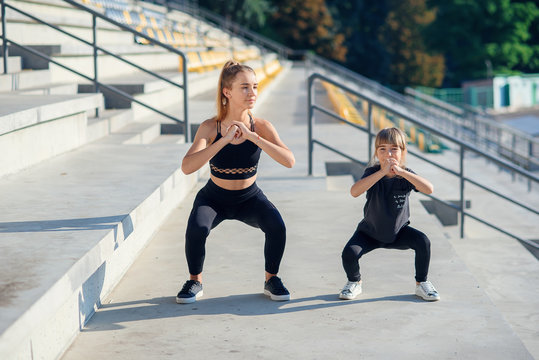 Sporty beautiful elder and younger sisters which squating together during fitness training outdoors. - Powered by Adobe