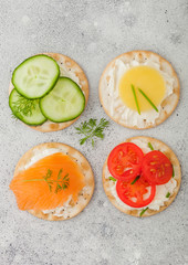 Various round healthy crackers with salmon and cheese, tomato and cucumber on light kitchen table background. Top view