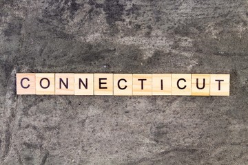 Connecticut word written on wood block, on gray concrete background. Top view.