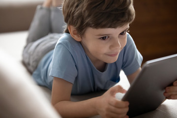 Smiling little school boy playing online game on computer tablet.
