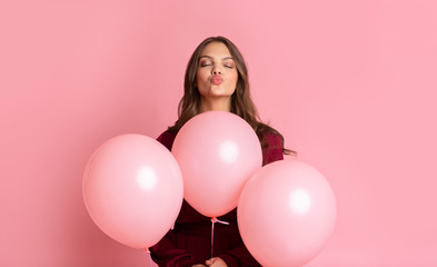 Fototapeta na wymiar Playful Girl Holding Rosy Balloons And Pouting Lips, Sending Air Kiss
