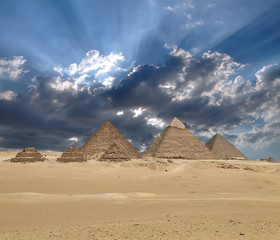 Sun shines from clouds above the Giza pyramid complex.