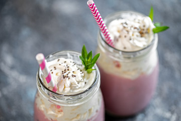 2 jars of milkshake or smoothie with cranberries, strawberries and blueberries standing on stone backdrop.