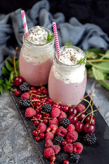 2 jars of milkshake or smoothie with cranberries, strawberries and blueberries standing on stone backdrop.