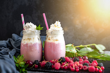2 jars of milkshake or smoothie with cranberries, strawberries and blueberries standing on stone backdrop.