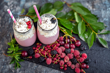 2 jars of milkshake or smoothie with cranberries, strawberries and blueberries standing on stone backdrop.