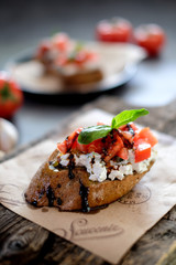 Bruschetta with tomato, basil and village cheese on wooden board with tomatoes background. Traditional italian appetizer or snack