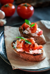 Bruschetta with tomato, basil and village cheese on wooden board with tomatoes background. Traditional italian appetizer or snack