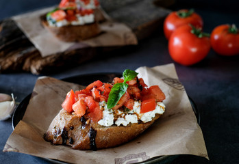 Bruschetta with tomato, basil and village cheese on wooden board with tomatoes background. Traditional italian appetizer or snack