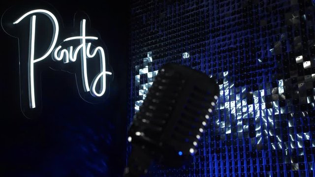 Concert vintage microphone on stage of nightclub party on shiny silver and neon sign background. Audio record equipment in music studio in dark blue light, occupation object for modern night lifestyle