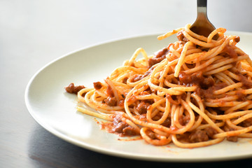 Spaghetti Bolognese with minced beef, onion, chopped tomato, garlic, olive oil, stock cube, tomato puree and Italian herb. Traditional Italian food in white plate with copy space. Selective focus. 
