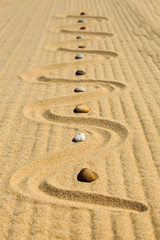 Auf Sandmuster angeordnete, bunte Steine am Strand, Land Art