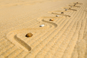 Fototapeta na wymiar Diagonal auf Sandmuster angeordnete, bunte Steine am Strand, Land Art