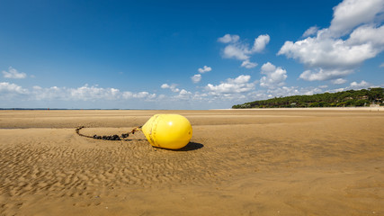 Gelbe Boje an einer Kette, die bei Ebbe im Sand liegt