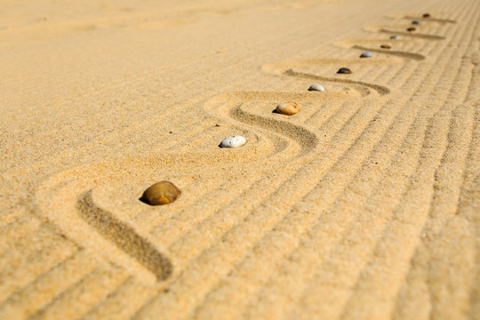 Diagonal auf Sandmuster angeordnete, bunte Steine am Strand, Land Art