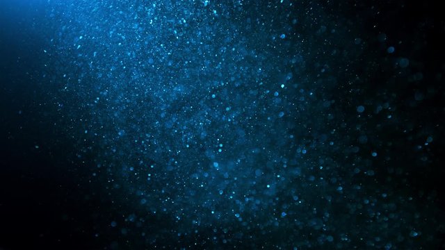 Blue glitter background in slow motion. Underwater particles flying and shining in bright spot light, shot with depth of field. Space dust beautiful bokeh abstract background