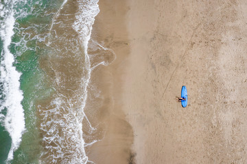 Surfer sitting on surf board on a beach from above