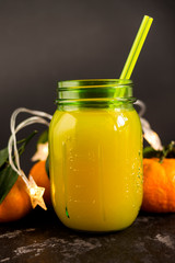 Freshly squeezed orange juice in a mason jar and fresh oranges fruit with green wet leaves on a black shabby background.