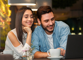 Boyfriend And Girlfriend Using Laptop Browsing Internet Sitting In Cafeteria