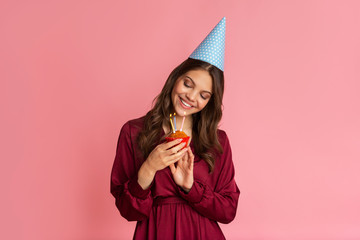 Young Girl In Birthday Hat Looking At Cupcake With Lighting Candles