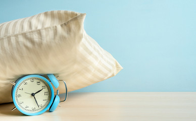 Morning Alarm clock under the pillow on the bedside table on blue wall background