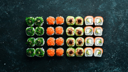 Big set of pieces of sushi rolls on black stone background. Top view. Free space for your text.