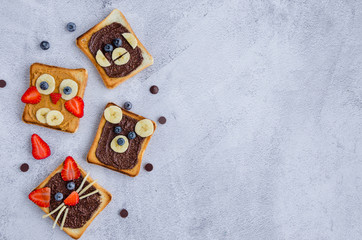 Healthy funny face sandwiches for kids. Animal faces toast with peanut and hazelnat chocolate butter, banana, strawberry and blueberry. Horizontal orientation. Copy space. Top view.
