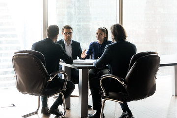 Confident businessman with colleague having heated discussion with partners sitting.