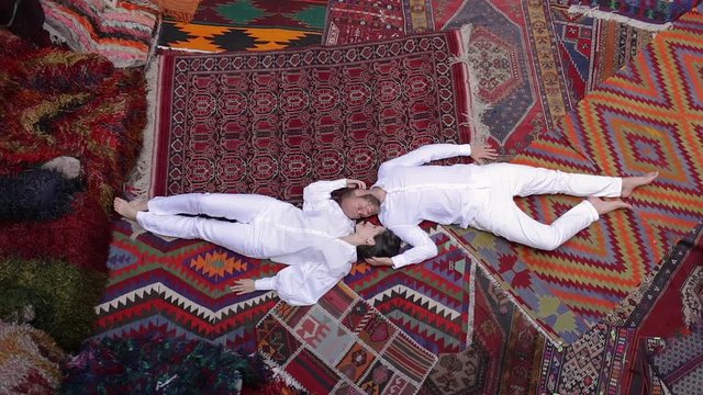 Young Happy Couple is Lying Down on the Floor and Laughing. Man Hugs the Girl. Cozy Colorful Carpet Room in Cappadocia