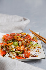 A plate with a Poke salad of seafood, rice and vegetables, avocado with soy sauce and Chia seeds on a grey cloth with Khasi sticks. A popular Hawaiian dish, flavorful, appetizing and healthy. 