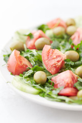 Salad with green Olives, Tomatoes, Cucumber and Rocket on bright Background. Healthy Snack Idea. Close up. 