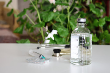 Against the background of plants, there is a bottle with a medical solution and a syringe with ampoules. In the background a stethoscope. Concept - health care, vaccination, protection against coronov