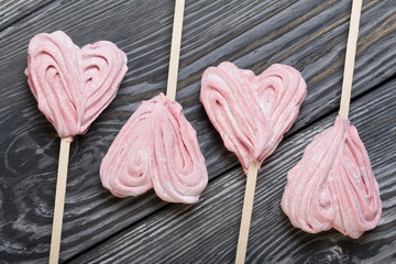 Delicate pink marshmallows in the shape of a heart on a stick. Several pieces lie in a row on brushed pine boards painted in black and white.