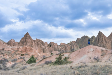 Person with hood and blue jacket is calmly with joy looking around the the landscape of red valley in Cappadocia. Tranquil and mystical peaceful places.