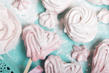 Delicate pink marshmallows of various shapes. Lies on a turquoise tray. Sprinkled with icing sugar.