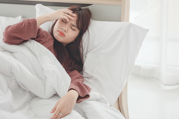 Asian woman feel headaches and discomfort on bed in white bedroom morning.Concept of women's health care.