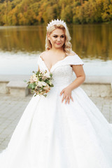 Fototapeta na wymiar Portrait of young bride with long hairs holding her wedding bouquet includes white roses and other flowers. Beautiful white marriage dress. Pretty girl on lake background