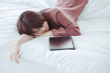 A woman playing a tablet on the bed in a white bedroom