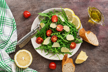 Easy diet healthy salad with arugula, tomato and parmesan on a dark background. Vegan and vegetarian lunch or dinner. Top view, flat lay.