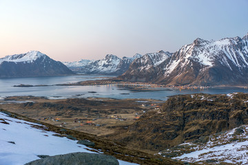 Landscape shot from Ryten towards fredvang and ramberg in Lofoten island in Norway during blue hour. Snow cover the peaks and city lights in the background.