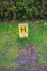 A concrete fire hydrant post with a yellow sign next to a metal drain cover with flaked yellow...