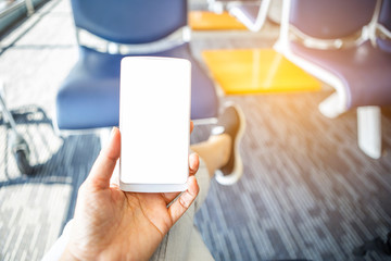 Smart phone with blank white screen in girl hand over blurred waiting seat at the airport, online travel booking 