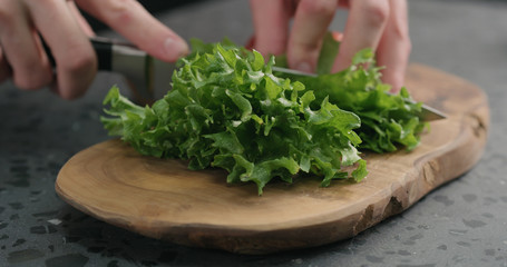man chopping frisee salad leaves on olive board